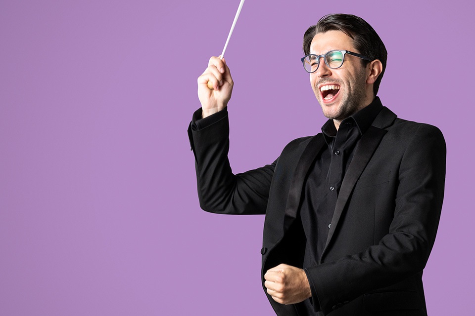 A student at the RCM conducting against a purple background